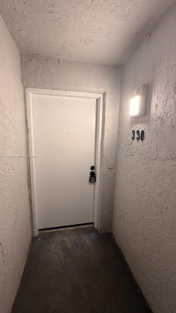 Exterior entryway featuring textured stucco walls, a solid-panel door, and a mounted square light fixture