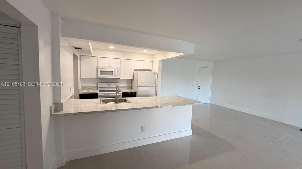 Kitchen featuring stone-patterned countertops, white cabinetry, integrated appliances, and a breakfast bar with an undermount sink
