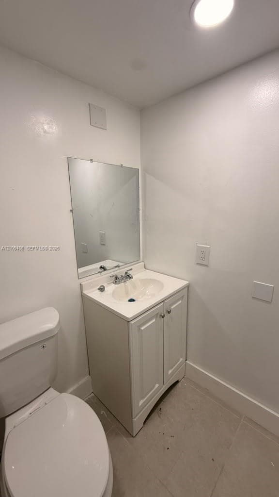 White bathroom vanity with a basin sink, chrome dual-handle faucet, rectangular wall-mounted mirror, and tile flooring
