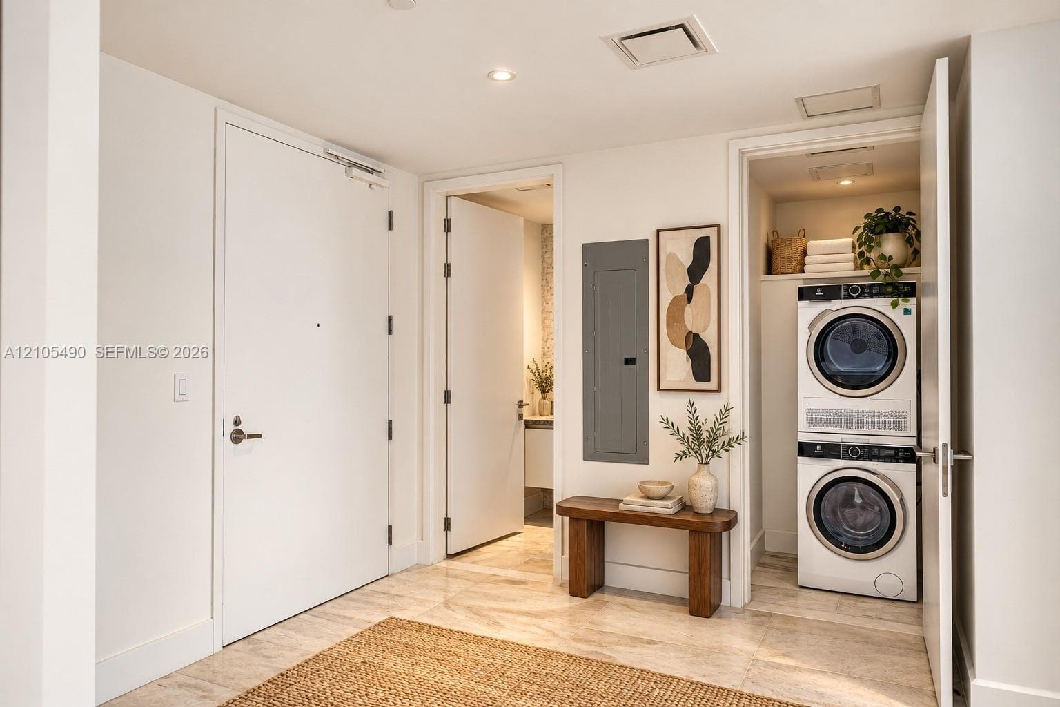 Neutral-toned stone flooring and recessed ceiling lighting throughout, featuring a dedicated laundry closet with a stacked washer and dryer, solid-core interior doors, and modern electrical panel