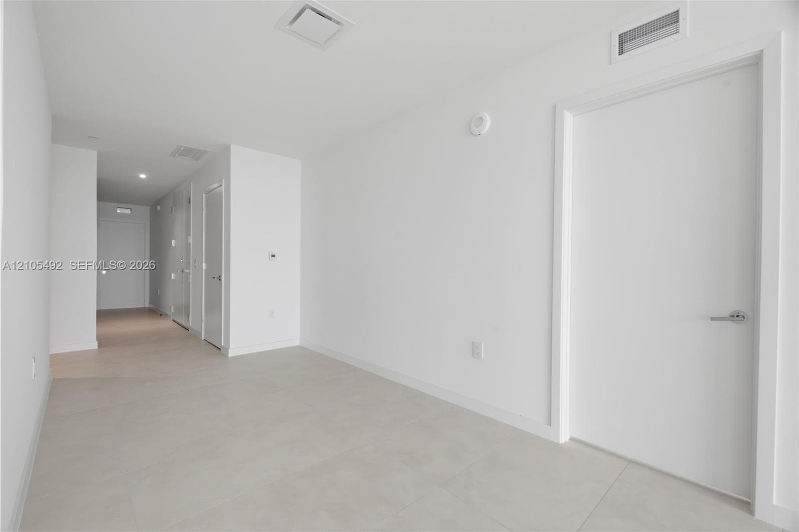 Interior space featuring large-format ceramic tile flooring, smooth white walls, solid-core interior doors with satin nickel hardware, and recessed LED ceiling lighting