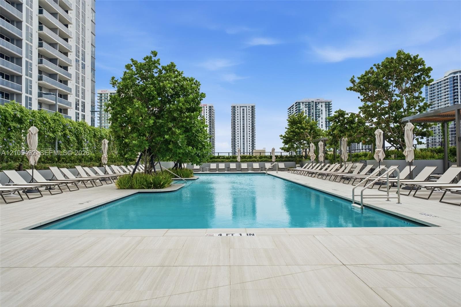 Swimming pool featuring a tiled deck, integrated metal handrails, and surrounding mature trees