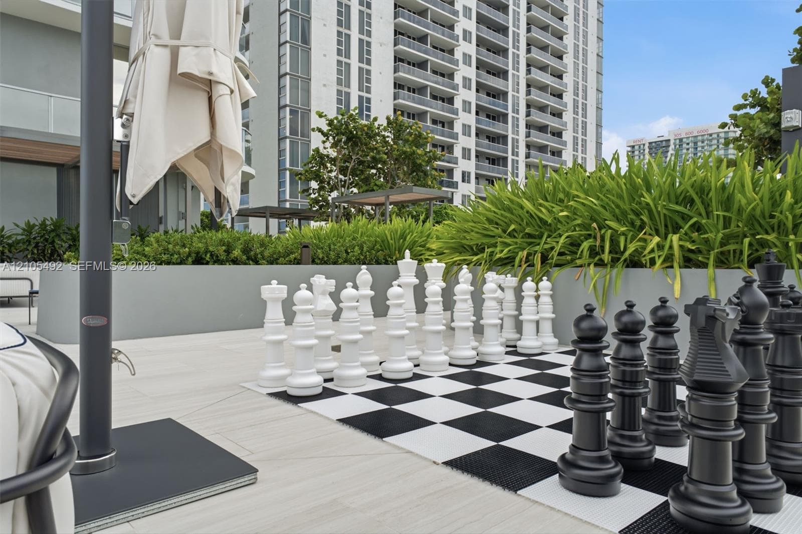 Outdoor terrace featuring a large-scale checkerboard, integrated raised garden planters with mature shrubbery, and light-toned tile flooring