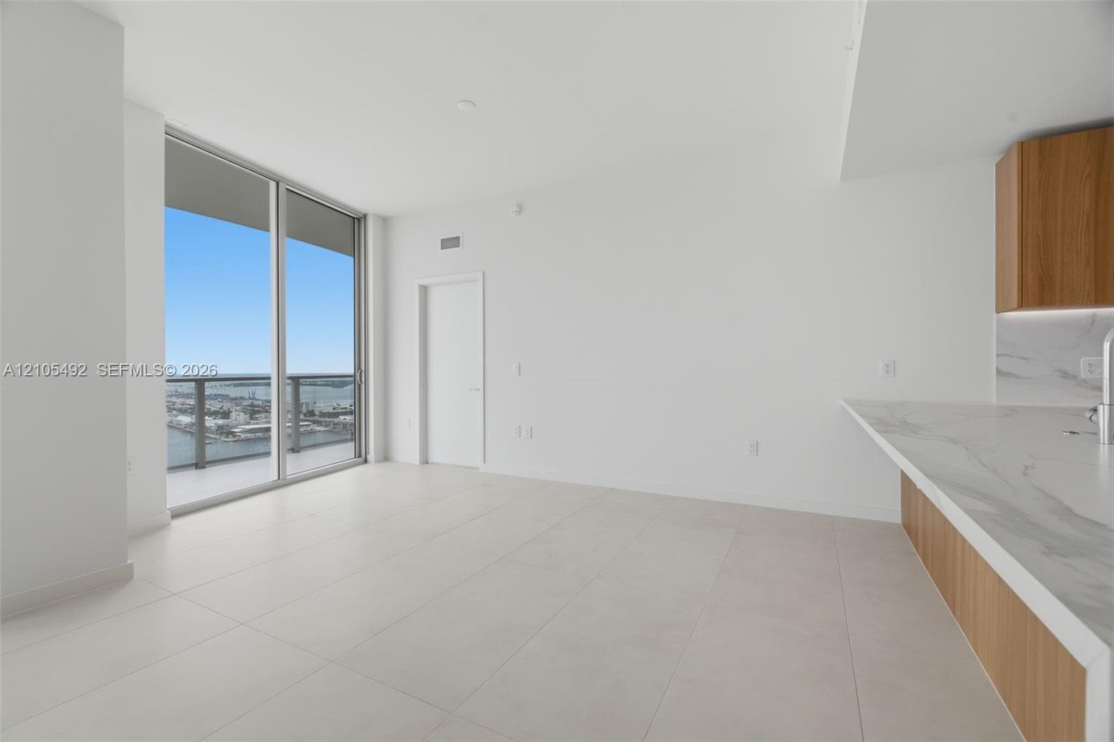 Floor-to-ceiling windows, light-tone tile flooring, stone-finish countertops, wood-finish cabinetry, and attached balcony