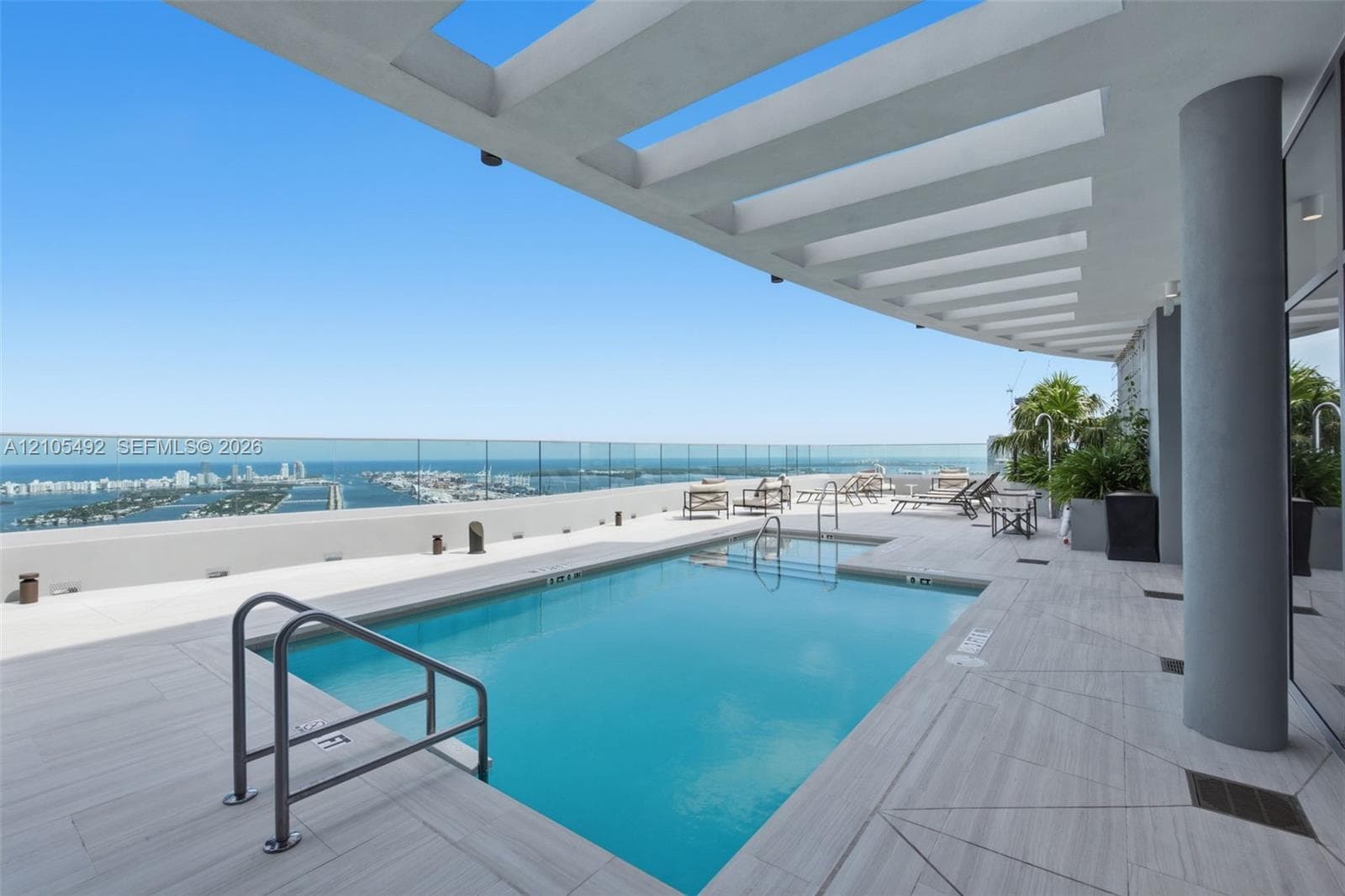 Rooftop swimming pool featuring wood-finish decking, a glass panel railing, and an overhead architectural trellis