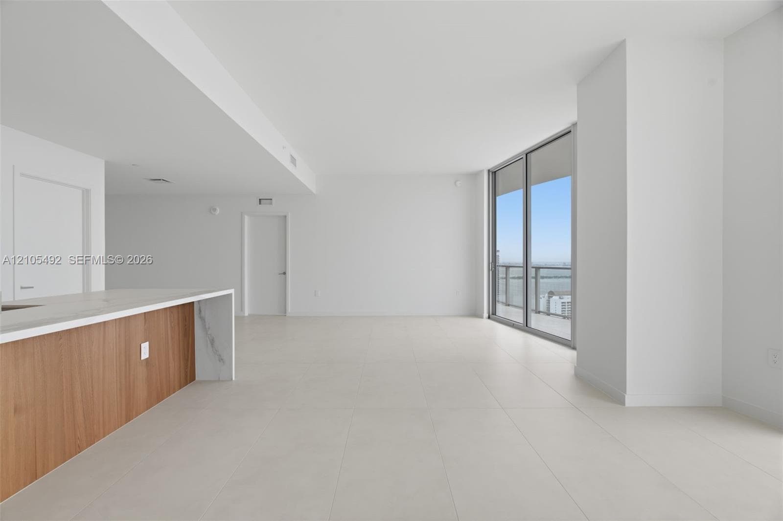 Open-concept interior featuring large-format tile flooring, floor-to-ceiling glass sliding doors, and a kitchen island with stone-finish countertops and wood-finish cabinetry