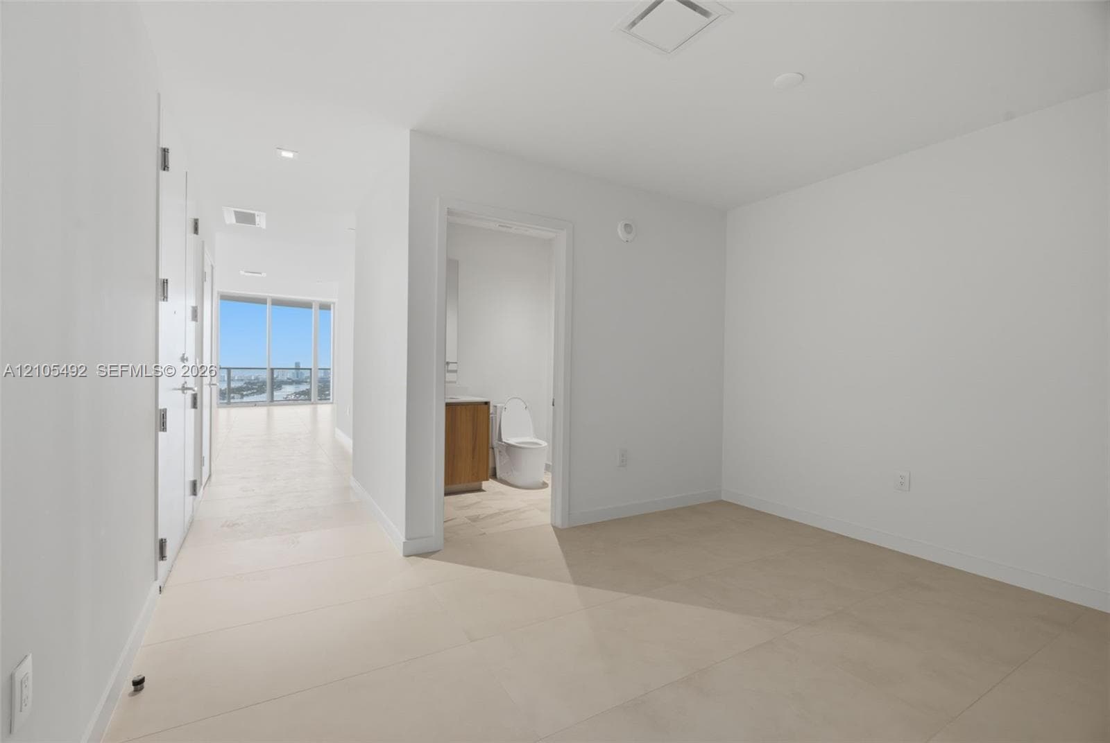 Interior space featuring neutral large-format tile flooring, recessed ceiling lighting, and a bathroom equipped with a wood-finish vanity and integrated toilet