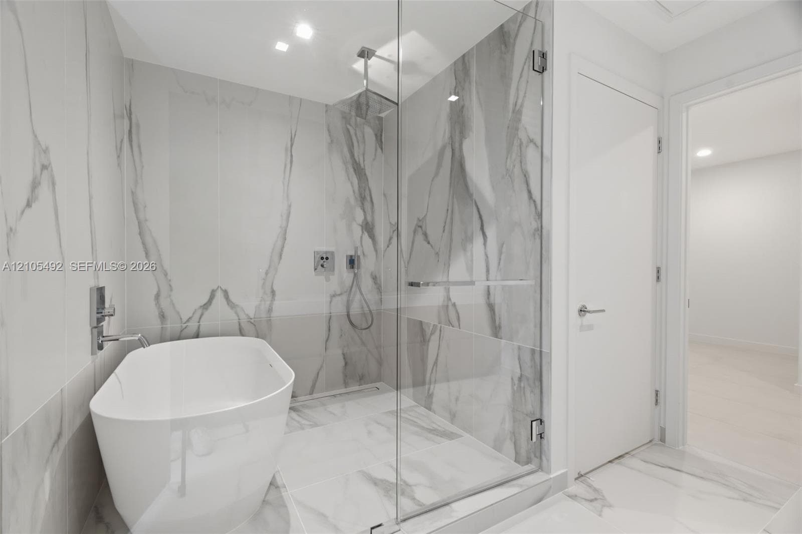 Freestanding soaking tub, frameless glass-enclosed shower, ceiling-mounted rainfall showerhead, and floor-to-ceiling stone-finish tile surround