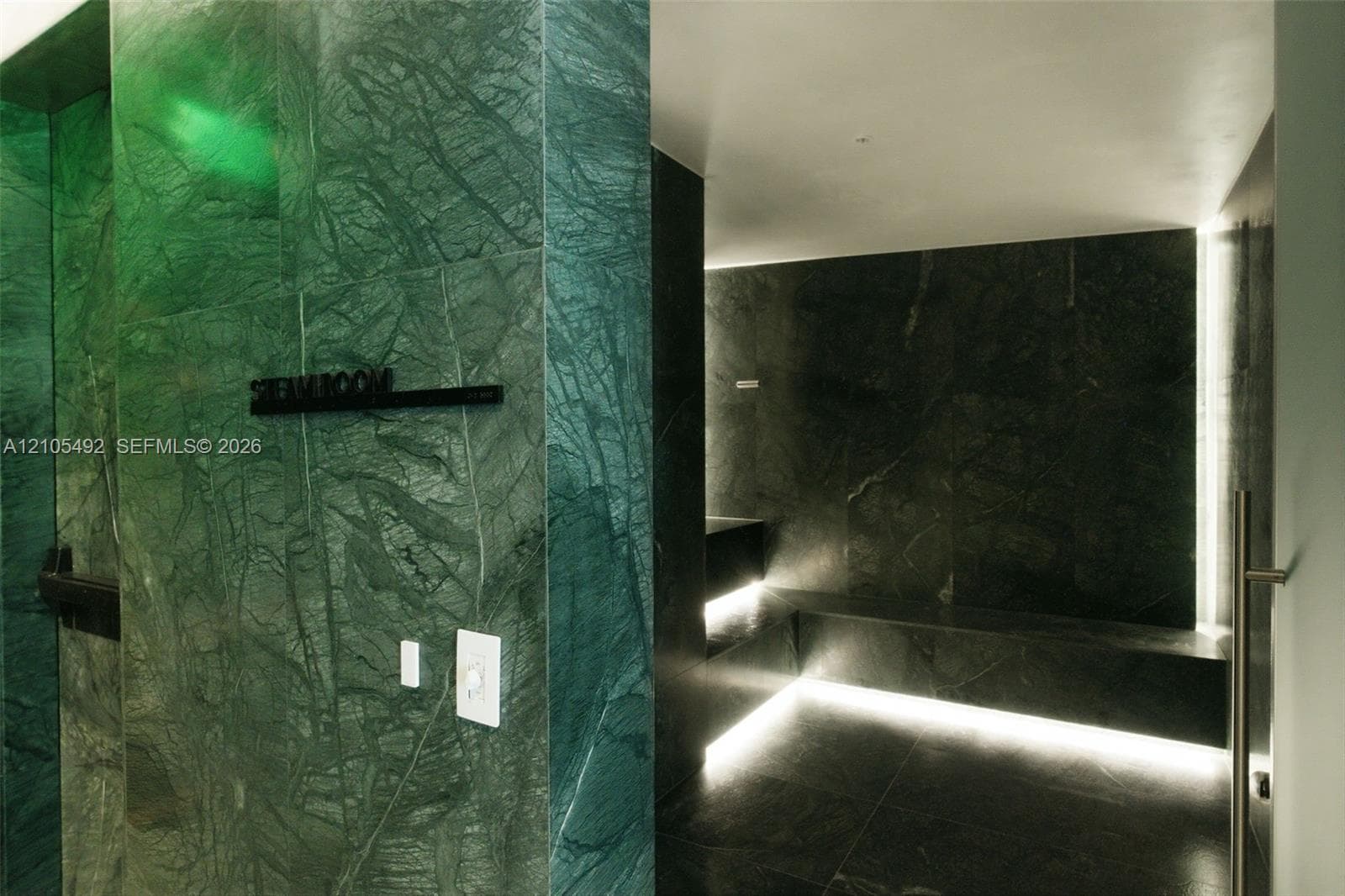 Steam room finished with large-format green stone slab wall cladding, integrated perimeter floor lighting, and built-in stone bench seating