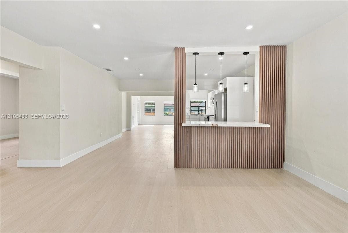 Kitchen pass-through featuring a white stone countertop, vertical wood-slat accent wall, three glass pendant lights, recessed ceiling lighting, and wood-finish flooring