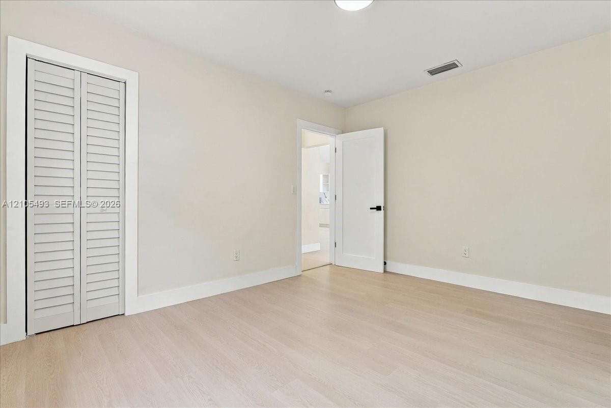 Neutral-toned interior featuring wood-finish flooring, white louvered bi-fold closet doors, and a solid-core interior door with matte black hardware