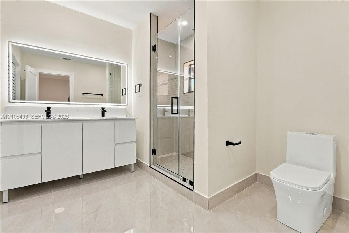 Floating double vanity with integrated sinks, LED-backlit mirror, glass-enclosed shower, and matte black fixtures