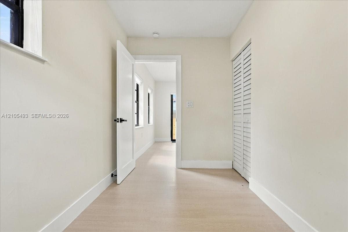 Interior space featuring neutral wall paint, wood-finish flooring, a white paneled door with matte black hardware, and white louvered closet doors