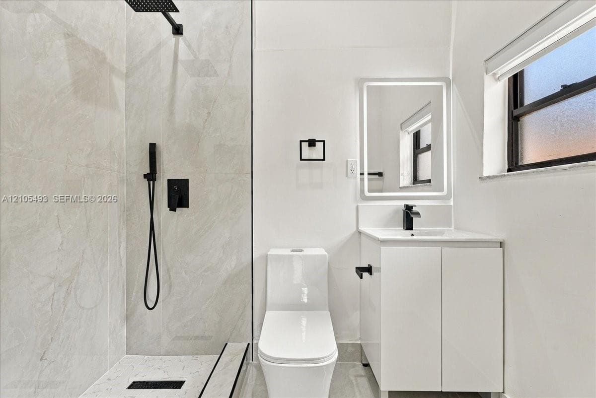 Bathroom featuring a glass-enclosed shower with matte black fixtures, rainfall showerhead, and floor-to-ceiling tile surround