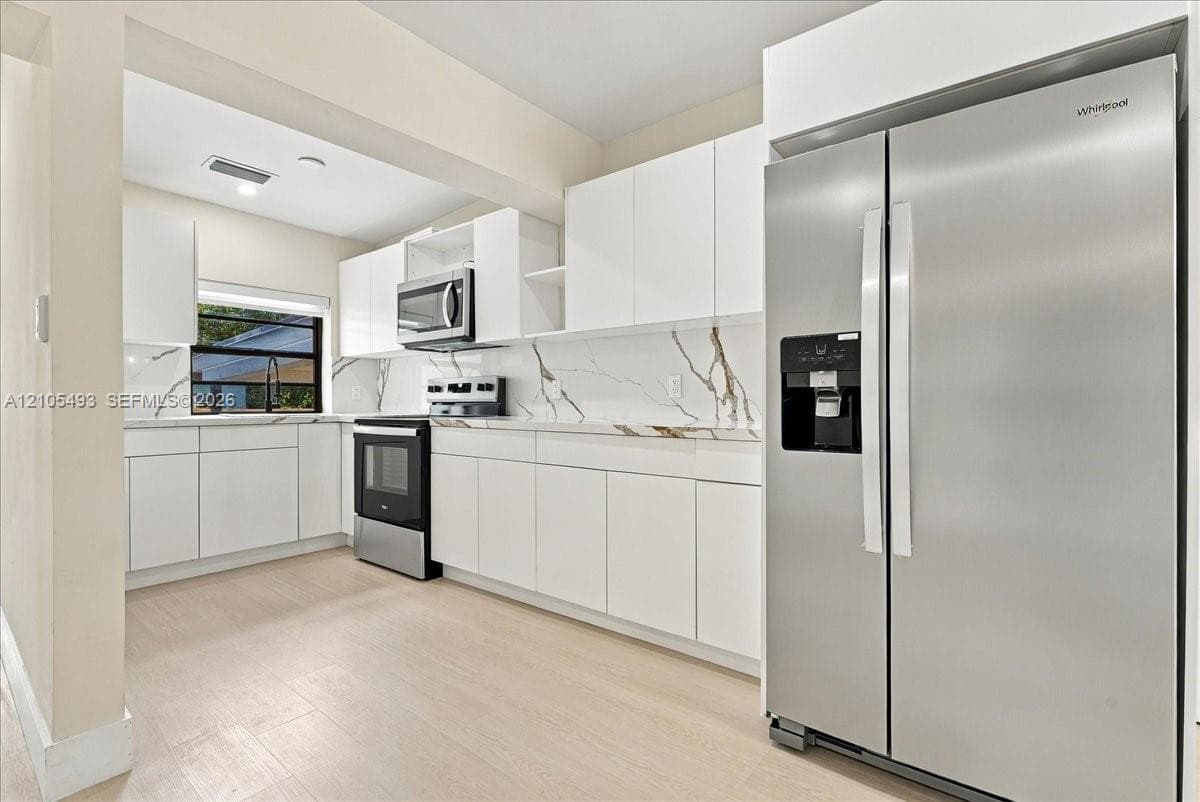 Kitchen featuring white cabinetry, stone-finish countertops with integrated backsplash, stainless steel appliances, and wood-finish flooring