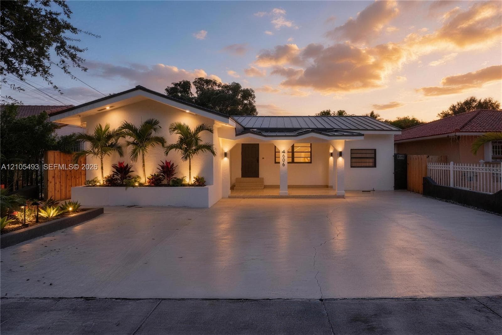 Single-story residence featuring a painted stucco exterior, metal roofing, covered entryway with arched support pillars, and integrated exterior landscape lighting