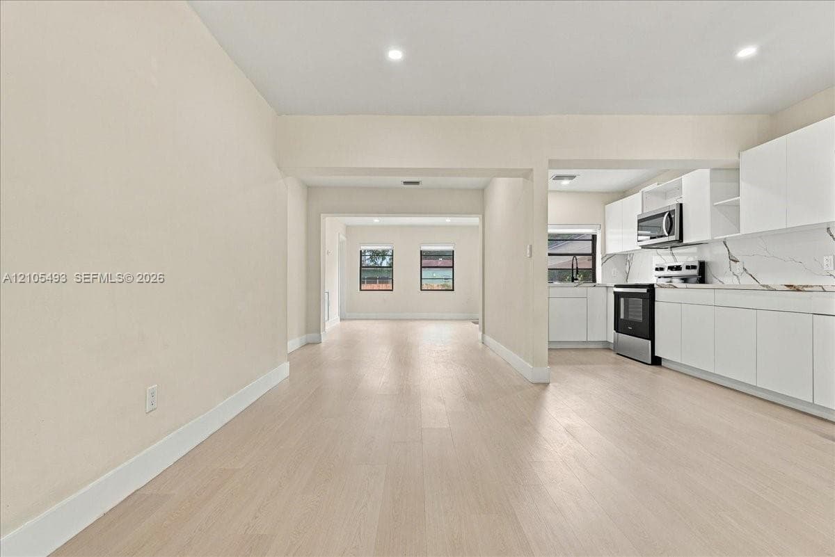 Kitchen featuring white cabinetry, stone-look countertops, stainless steel microwave, and wood-finish flooring throughout