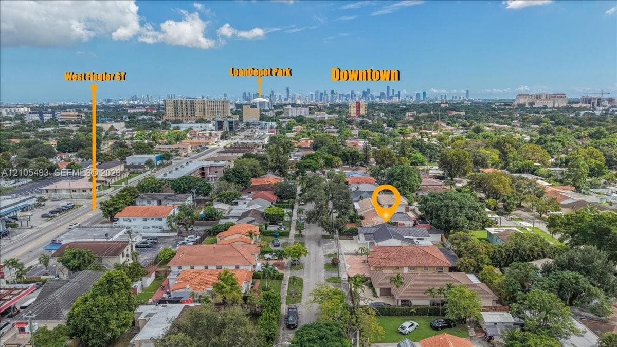 Aerial perspective showcasing a residential lot with a tile-roof structure and mature trees, positioned in an urban environment with an expansive metropolitan skyline background