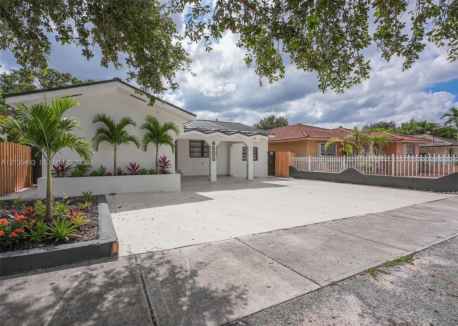 Exterior featuring a white stucco facade, a decorative covered entryway with a scalloped roofline, a paved concrete driveway, and tiered planter boxes