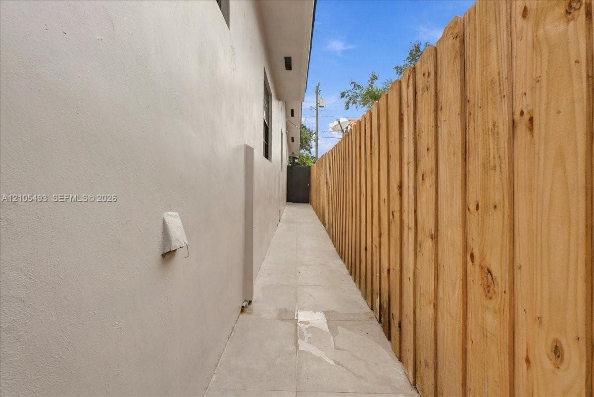 Side yard featuring smooth stucco exterior siding, concrete paving, and a tall wood privacy fence