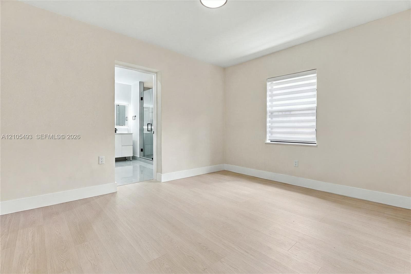 Neutral-toned interior space featuring light wood-finish flooring, a single-window configuration with horizontal blinds, and recessed ceiling lighting