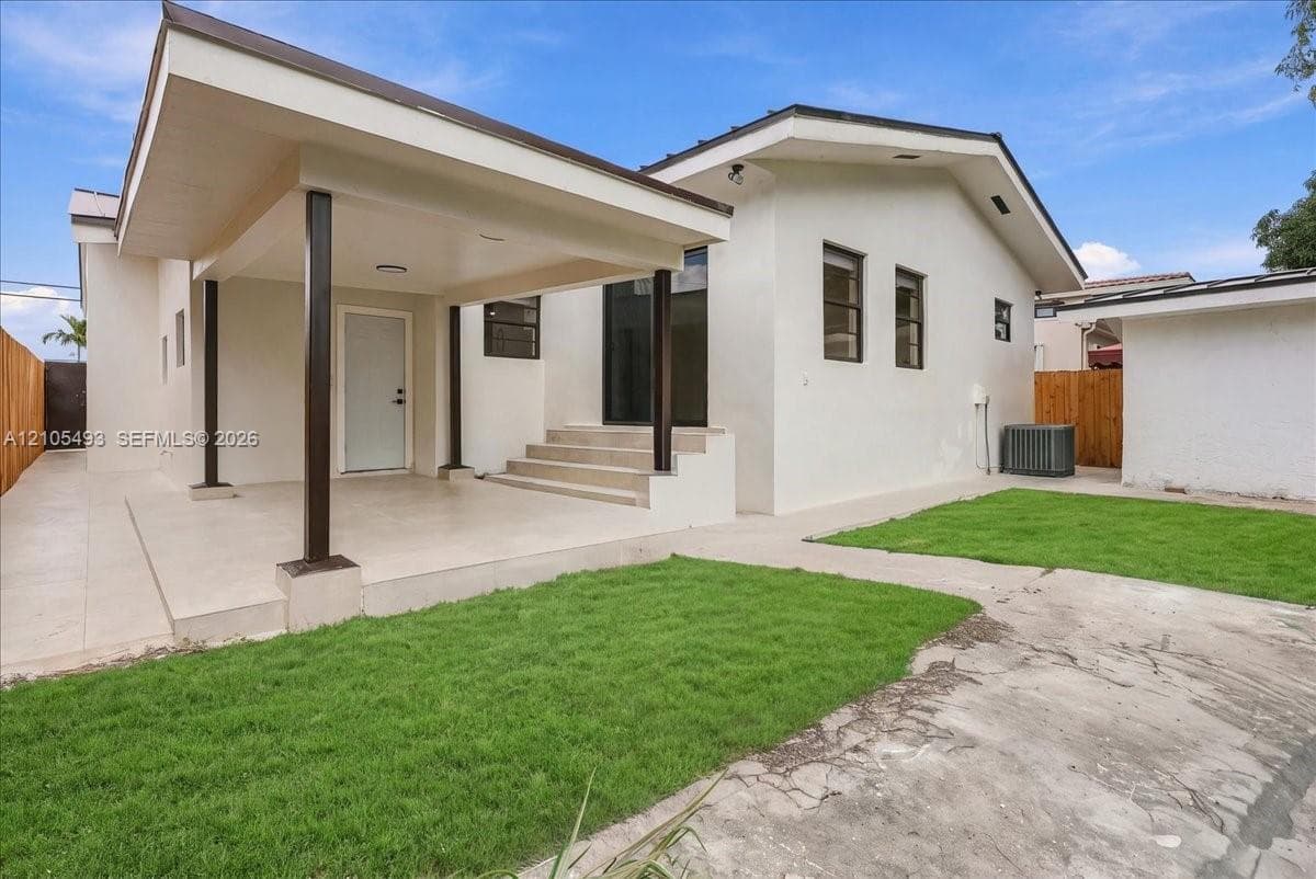Stucco exterior featuring a covered patio, concrete hardscaping, tiered stairs, and wood-toned fencing