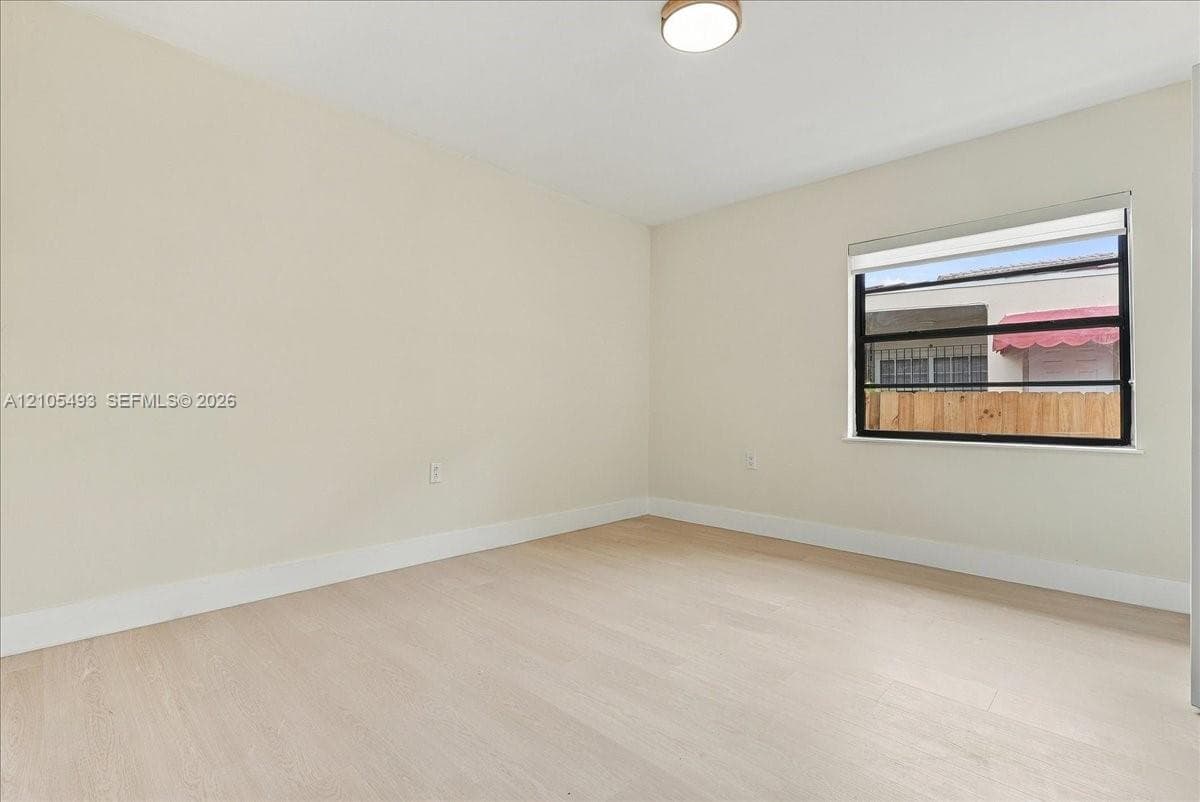 Neutral interior featuring wood-finish flooring, light-toned walls, a single-pane horizontal window with a fitted roller shade, and a flush-mount overhead light fixture