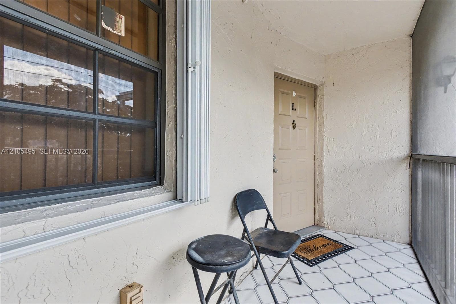 Screened porch entry featuring white hexagonal tile flooring, a multi-pane grid window, and a paneled door with a metal knocker