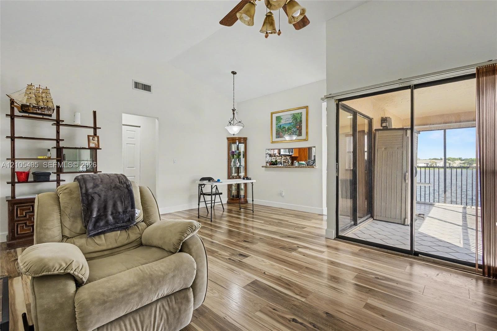 Open-concept area featuring vaulted ceilings, wood-finish flooring, a pass-through window to the kitchen, and sliding glass doors with water exposure
