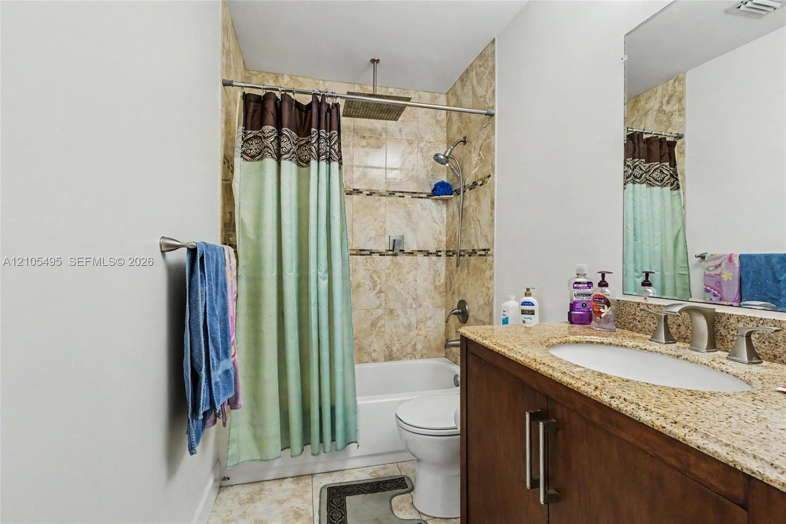 Bathroom featuring a dark wood-finish vanity with a stone countertop, an integrated oval sink, a shower-tub combination with stone-tile surround, and a rainfall showerhead