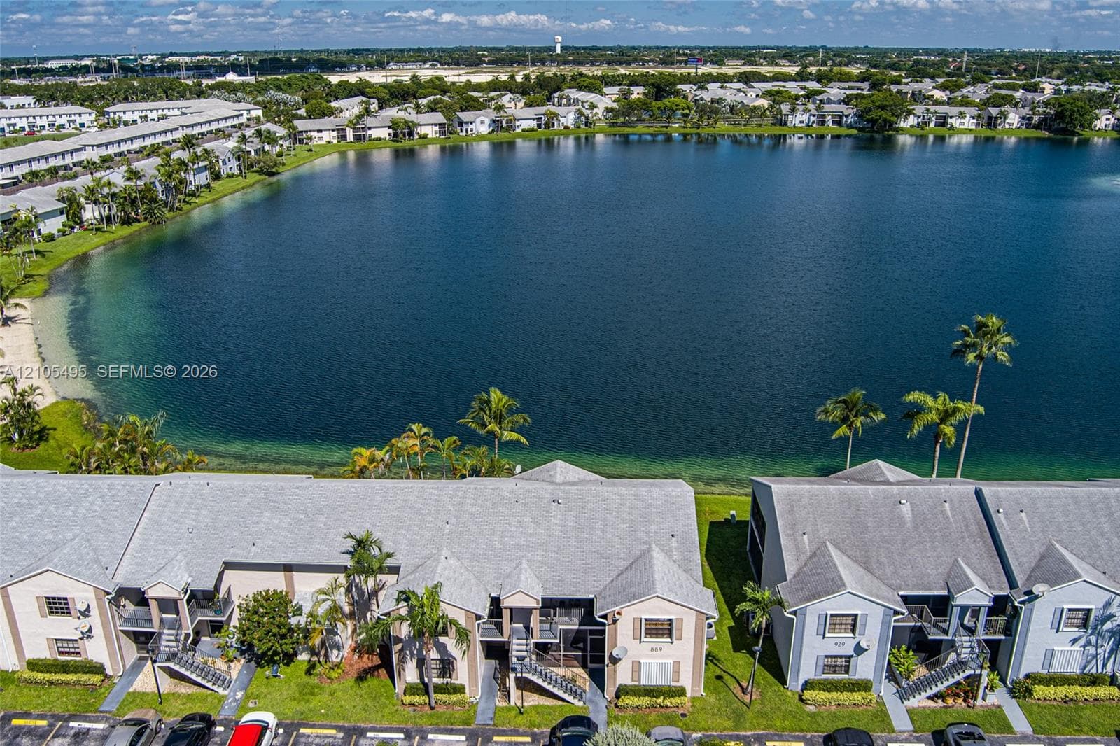 Aerial perspective featuring multi-story residential buildings with shingled rooflines, situated along a expansive lakefront shoreline with mature palm trees