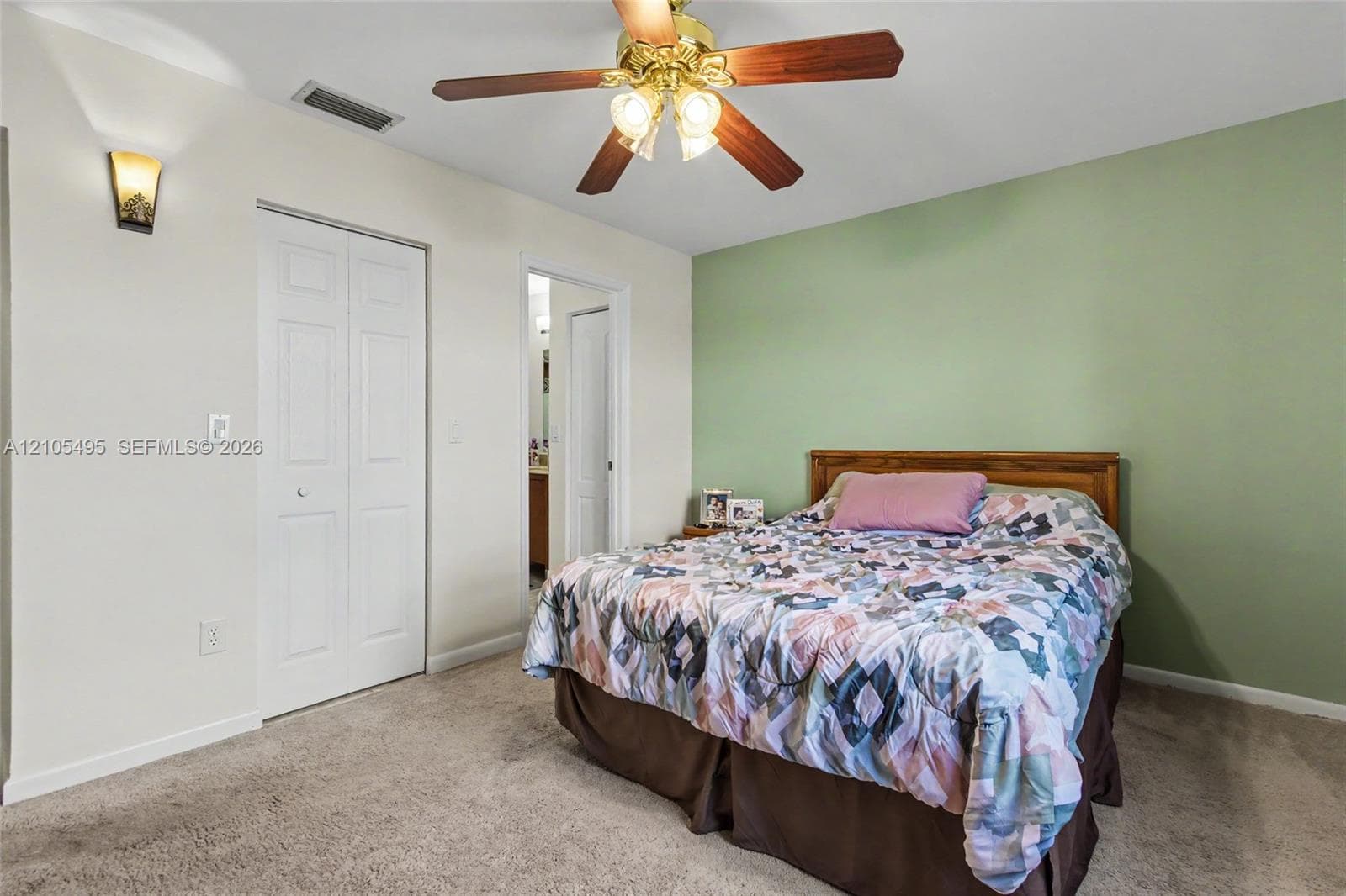 Neutral-toned interior space featuring a ceiling fan with integrated lighting, wall-mounted accent sconce, bi-fold closet doors, and carpeted flooring
