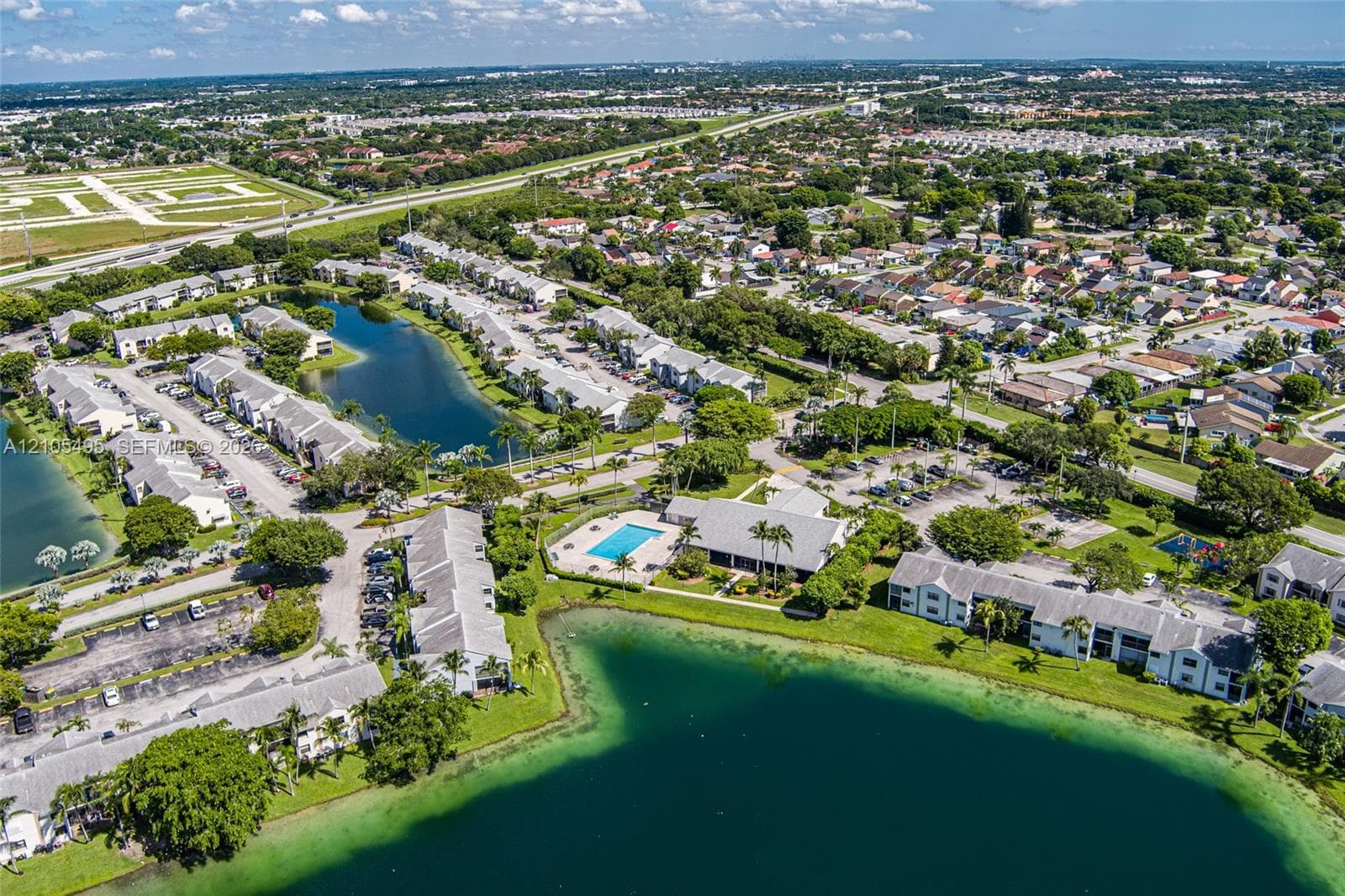 Aerial perspective of a multi-unit residential community featuring waterfront positioning, a centralized swimming pool, paved surface parking, and manicured landscaping