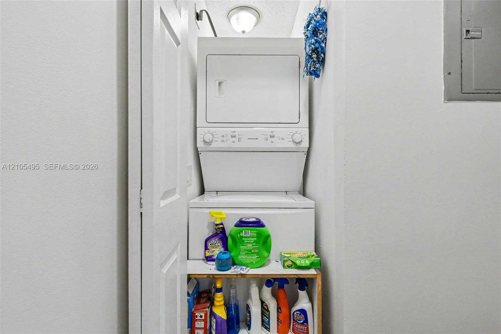 Stacked laundry unit featuring white enamel finish, ceiling-mounted light fixture, and dedicated closet space with bi-fold door