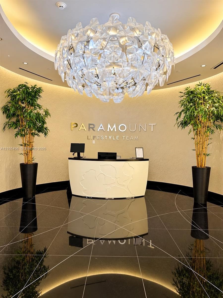 Rotunda entry featuring a large sculptural chandelier, polished black stone flooring with linear inlay patterns, textured wall finishes, and a custom curved built-in reception desk