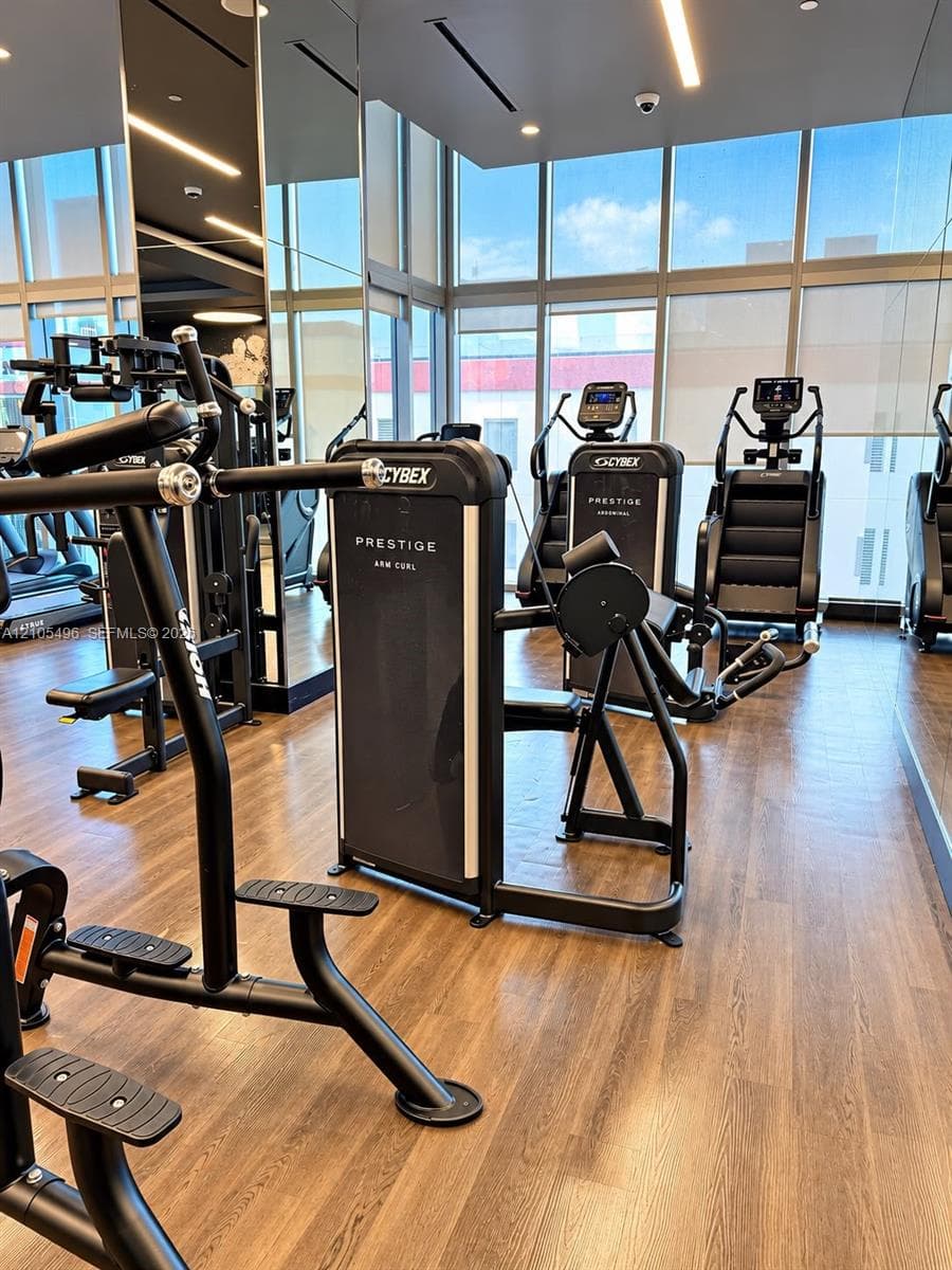 Fitness center featuring floor-to-ceiling windows, wood-finish flooring, recessed lighting, and mirrored wall surfaces