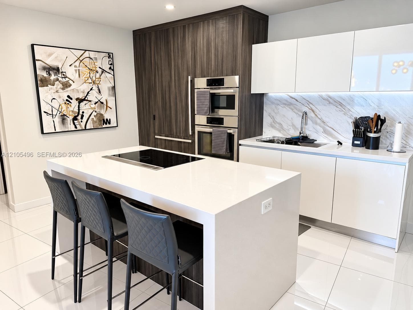 Kitchen featuring a waterfall-edge island with an integrated cooktop, flat-panel cabinetry, a stone-pattern backsplash, and stainless steel built-in appliances