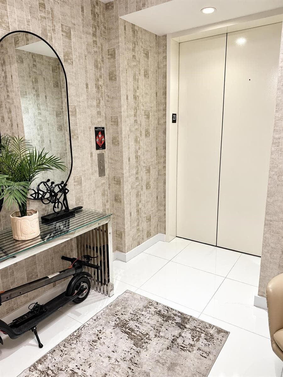 Private elevator access featuring floor-to-ceiling high-gloss finish doors, polished tile flooring, and textured wall coverings with recessed lighting