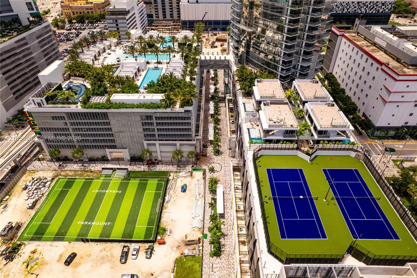 Aerial perspective of building complex featuring rooftop swimming pools, tennis courts, and a synthetic turf athletic field
