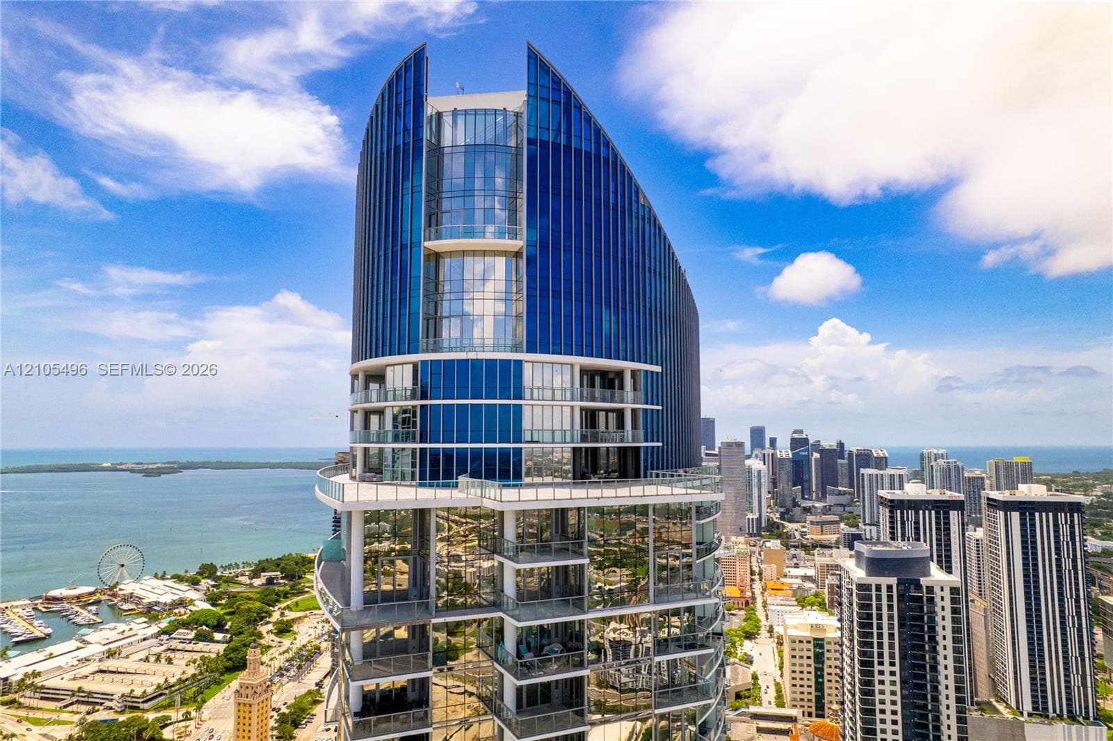 High-rise structure featuring blue glass curtain walls, curved architectural design, and multiple levels of private balconies