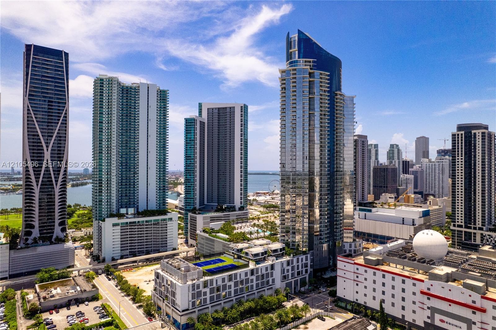 High-rise residential exterior featuring a reflective glass facade, tiered architectural design, and a rooftop sports court