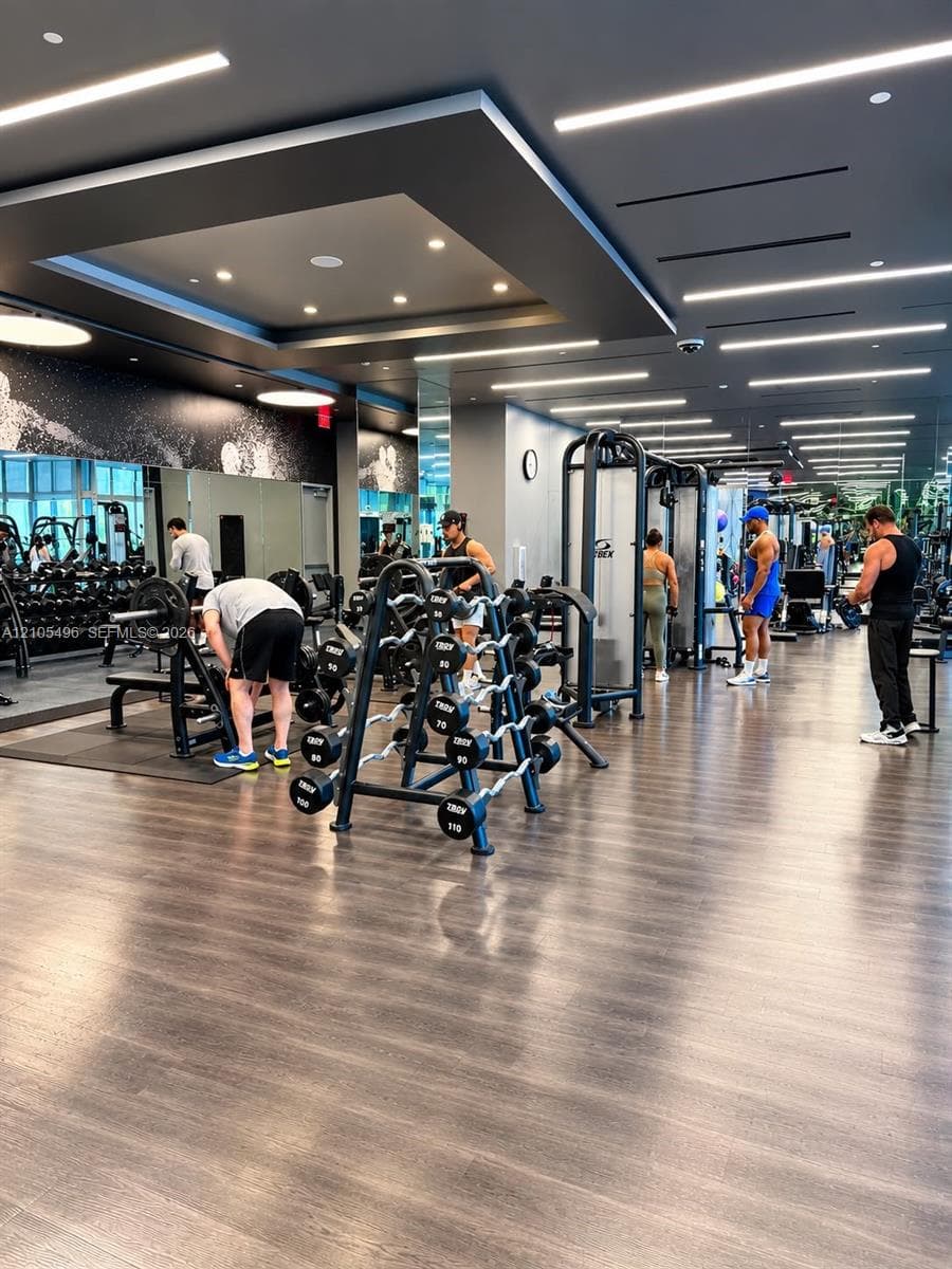 Fitness center featuring wood-finish flooring, a recessed tray ceiling with integrated linear lighting, and wall-to-wall mirrors
