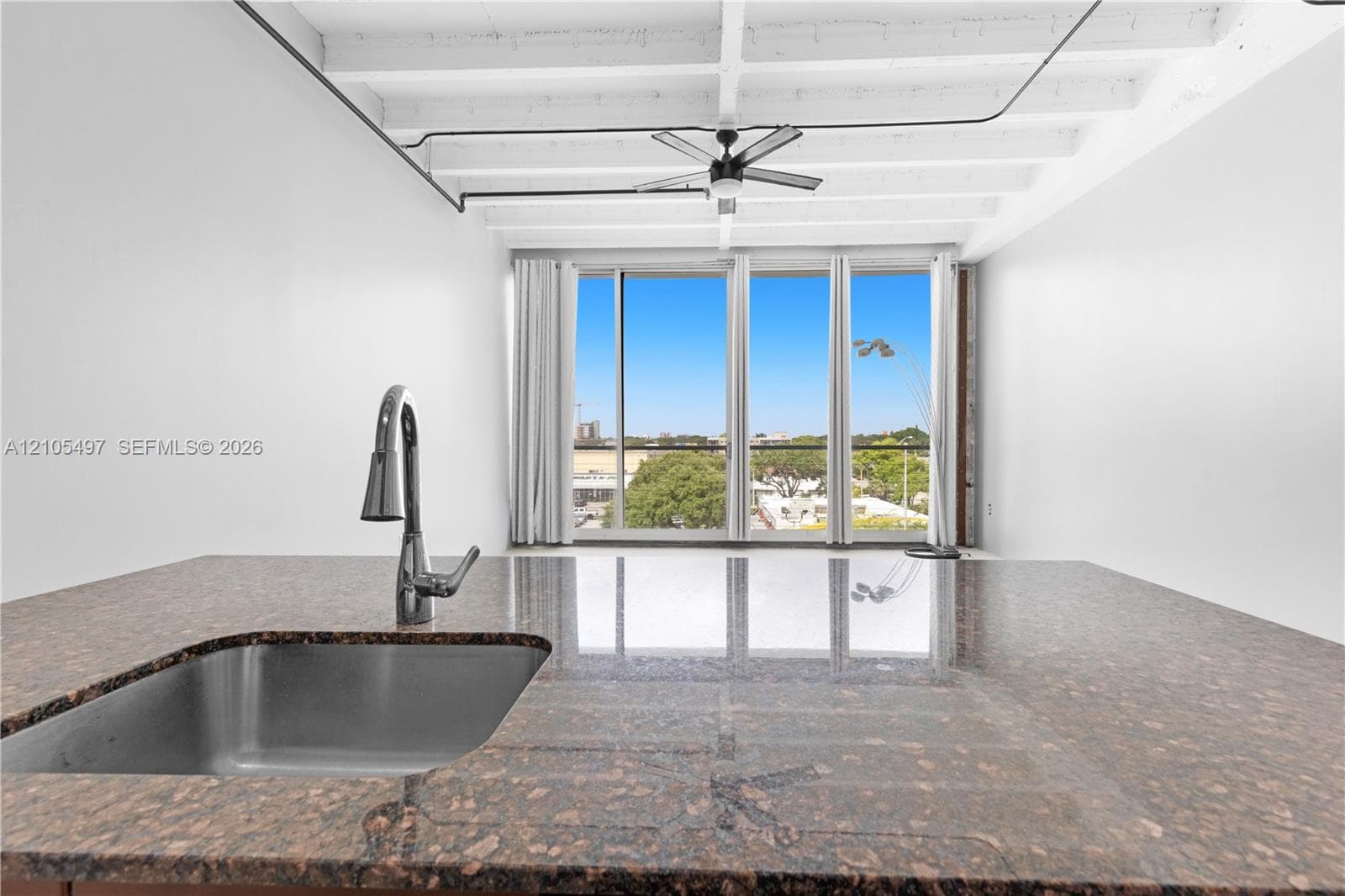 Integrated stainless steel sink with a high-arc faucet, granite-finish countertop, exposed ceiling beams, and full-height windows