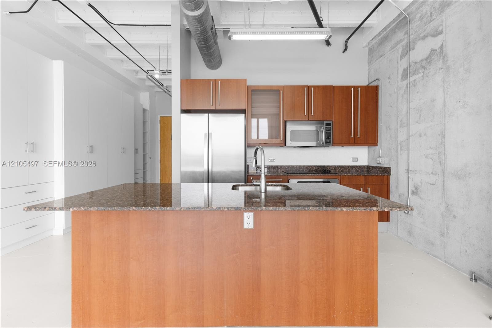 Kitchen island with granite countertop, stainless steel appliances, and wood-finish cabinetry