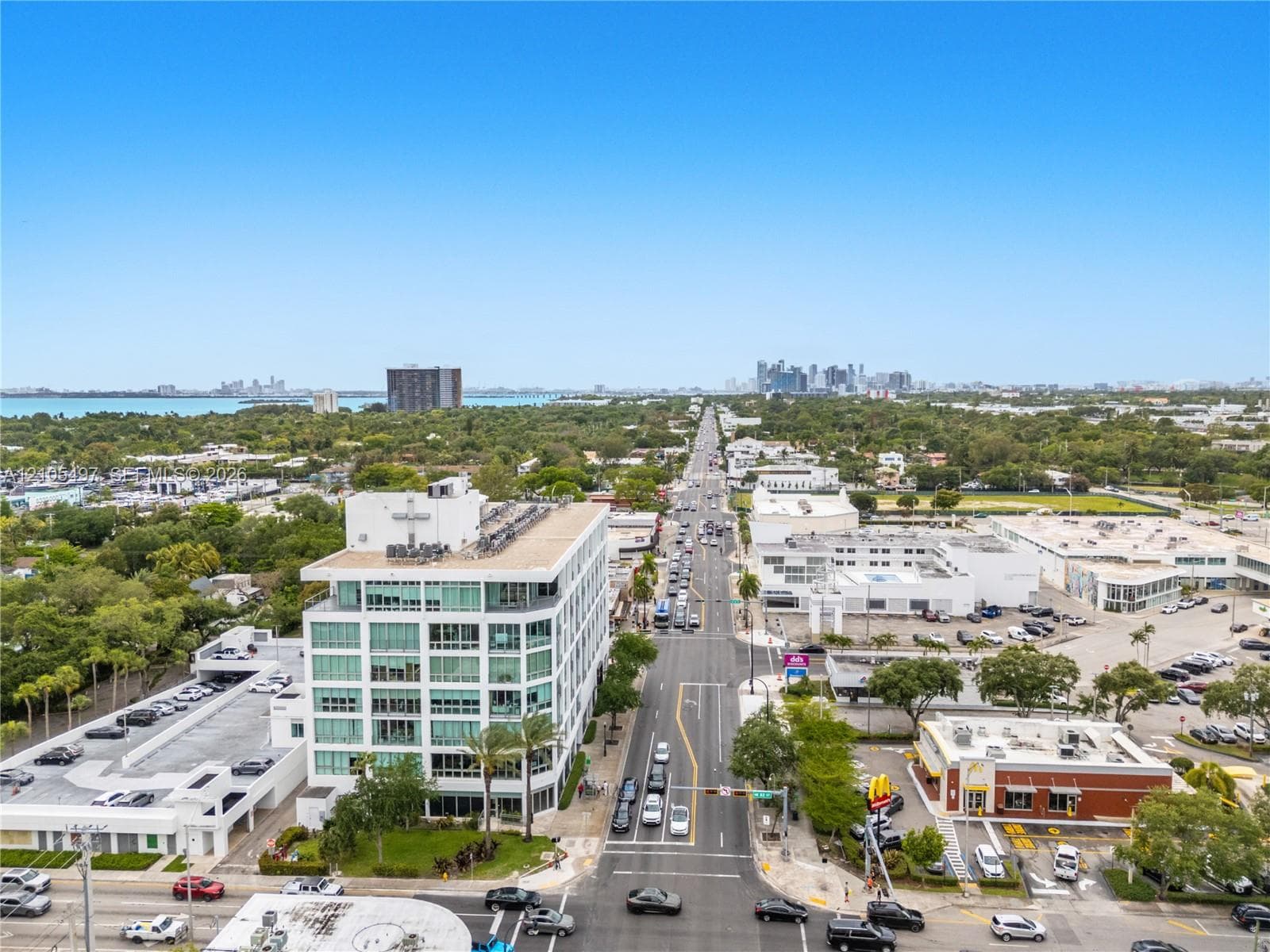 Aerial perspective showcasing a structured streetscape with a prominent multi-story building, an expansive parking structure, and distant water scenery