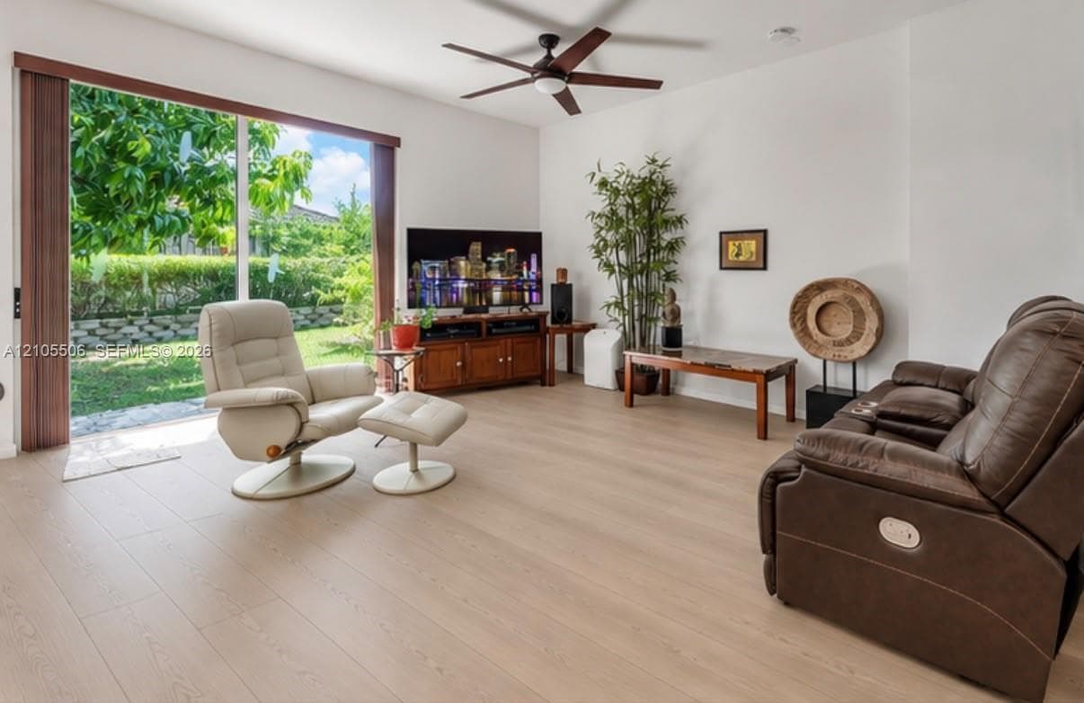 Expansive sliding glass door, light wood-finish flooring, white walls, and a ceiling fan with integrated lighting