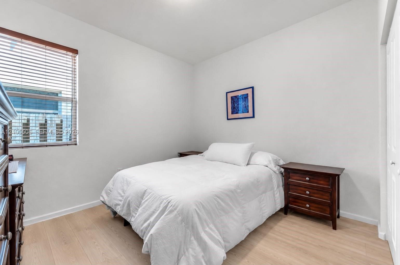 Light wood-finish flooring with white walls and a window featuring horizontal blinds