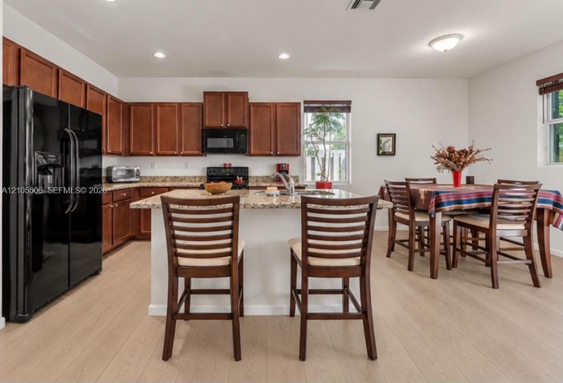 Kitchen featuring wood-finish flooring, granite countertops, wood cabinetry, and a kitchen island with seating