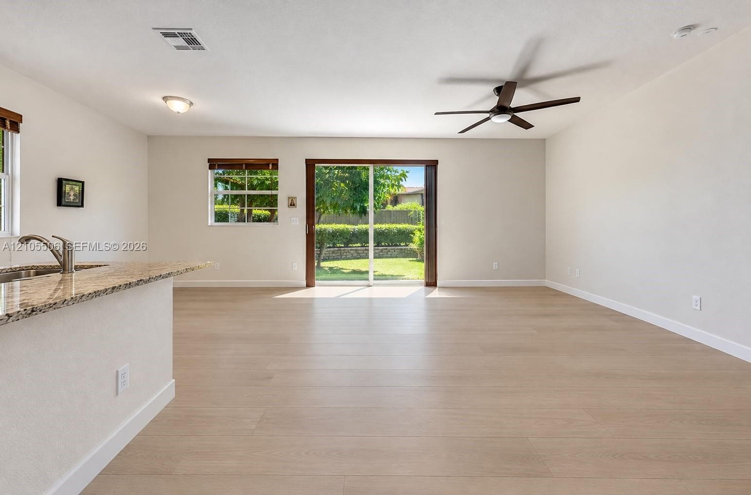 Light wood-finish flooring throughout, featuring a ceiling fan, recessed lighting, and a sliding glass door providing outdoor access