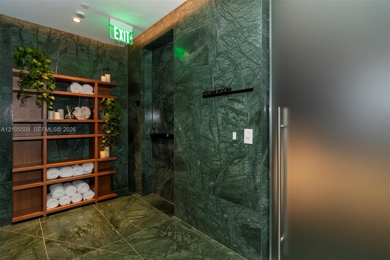 Green stone tiled walls and flooring, wood-finish shelving, and a frosted glass door with a metal handle